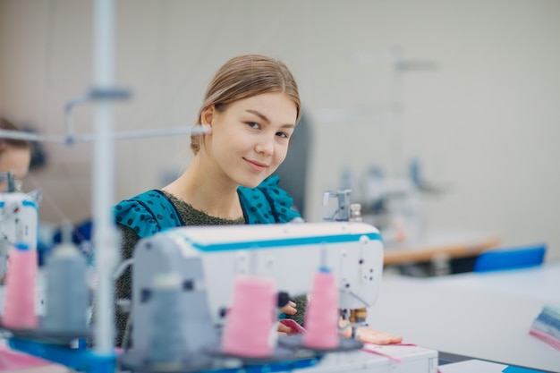 Costurera hermosa joven cose en la máquina de coser en la fábrica