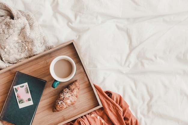 Croissant y café cerca del libro en la cama Foto gratis