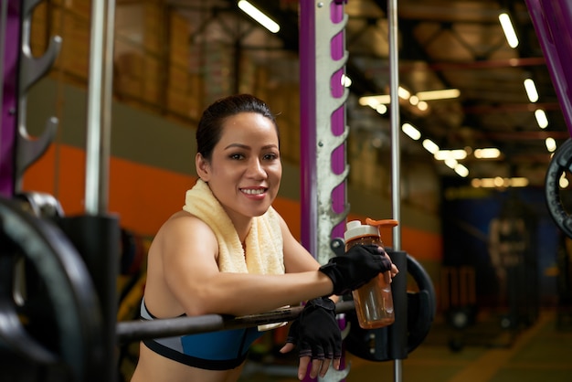 Deportista alegre sonriendo a la cámara en la máquina smith en un gimnasio Foto gratis