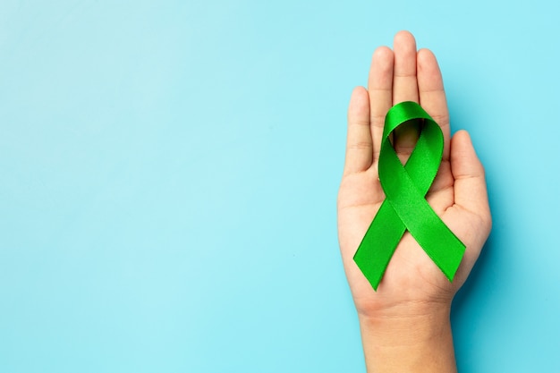 Día mundial de la salud mental. cinta verde puesta en la mano del ser  humano sobre fondo azul. | Foto Gratis