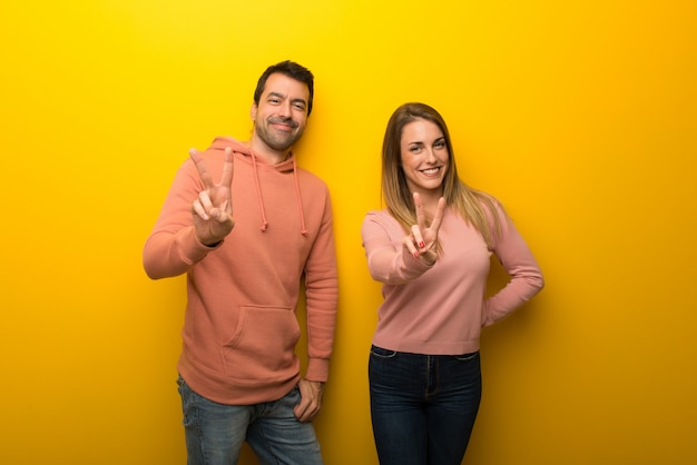 En el día de san valentín grupo de dos personas sobre fondo amarillo  sonriendo y mostrando el signo de la victoria | Foto Premium