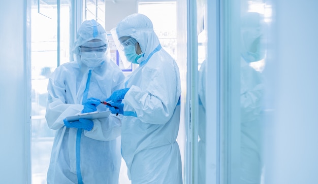 Doctora asiática en traje de protección personal con máscara de escritura en el cuadro de cuarentena del paciente, sosteniendo un tubo de ensayo con muestra de sangre para detectar el coronavirus. coronavirus, concepto covid-19. Foto Premium 