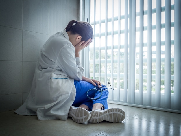 Doctora deprimida sentada en la desesperación cerca de una ventana del hospital - concepto de salud y dolor Foto gratis
