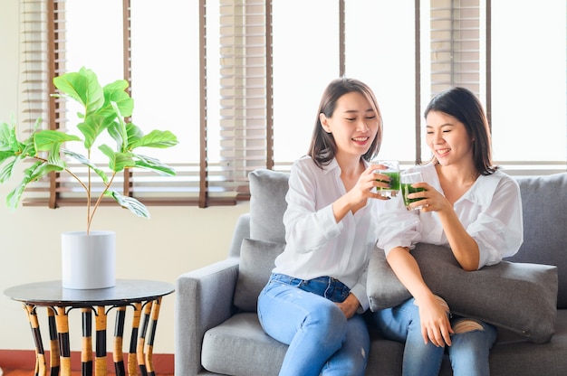 dos amigas asiáticas felices disfrutan bebiendo jugo verde juntos en la