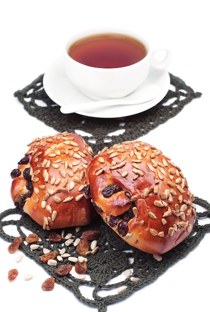 Dos bollos con pasas y semillas de girasol y una taza de té sobre fondo