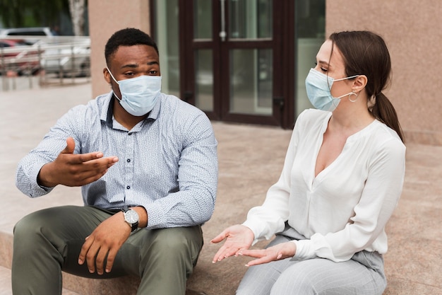 Dos colegas charlando al aire libre durante la pandemia con máscaras Foto gratis