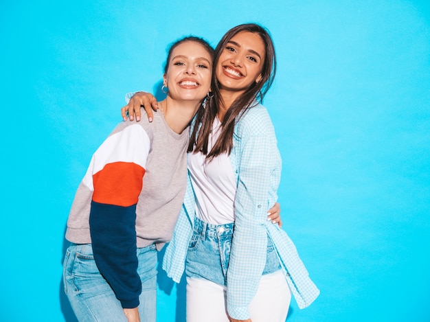 Dos jóvenes hermosas sonrientes rubias hipster chicas en ropa de verano colorida camiseta. mujeres despreocupadas sexy posando junto a la pared azul. modelos positivos divirtiéndose Foto gratis