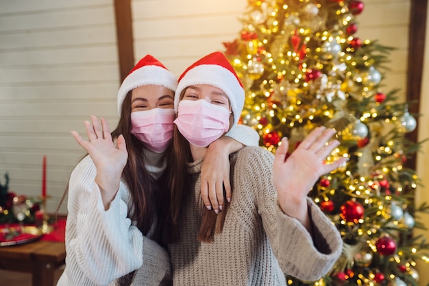 Dos niñas con máscaras protectoras mirando a la cámara y saludando. navidad durante el coronavirus, concepto Foto gratis