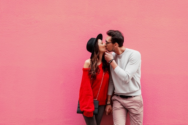 Elegante elegante pareja de enamorados cogidos de la mano y mirándose con placer. mujer de pelo largo en suéter de punto rojo con su novio posando. Foto gratis