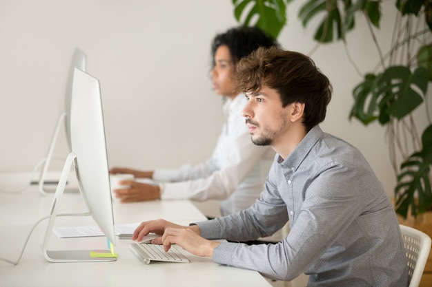 Empleado serio joven enfocado en trabajo de computadora en oficina multirracial Foto gratis