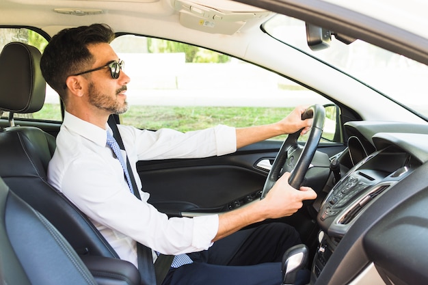 Empresario elegante con gafas de sol conduciendo el coche Foto gratis