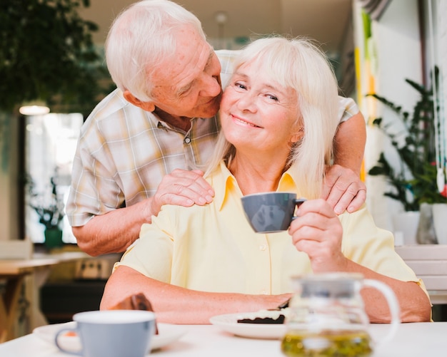 Encantado Pareja De Ancianos Sentados En La Cafetería Y Besos Foto Gratis 