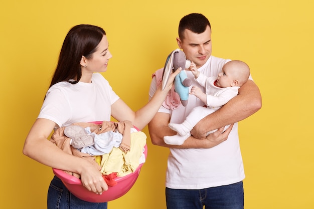 Encantadora Familia Joven De Tres Siendo Fotografiada Contra La Pared Amarilla Mama Haciendo Landry Y Sosteniendo