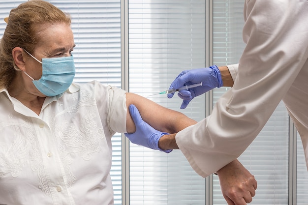 Enfermera con una jeringa sosteniendo el brazo de una anciana con una máscara para ser vacunada Foto Premium 
