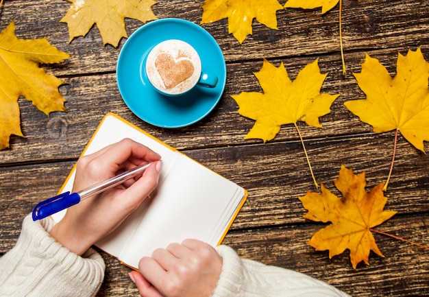 Escritura femenina de la mano algo en cuaderno cerca de la taza de café