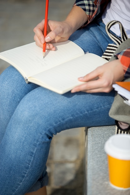 Estudiante dama escribiendo en un cuaderno abierto con un lápiz | Foto