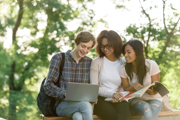 Estudiantes felices sentados y estudiando al aire libre ...