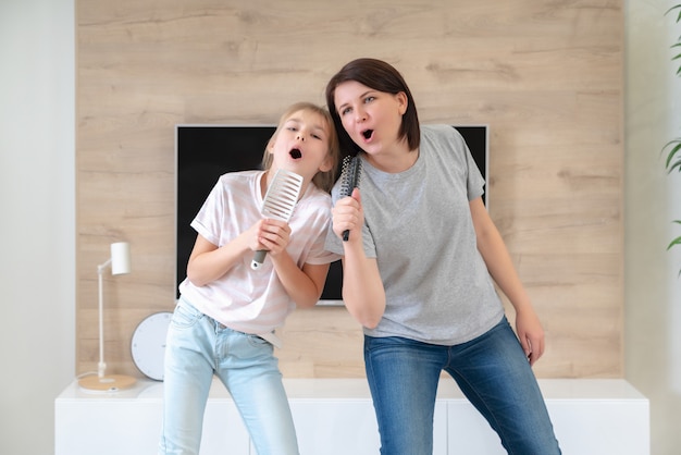 Familia feliz madre adulta joven y linda hija adolescente divirtiéndose  cantando canciones de karaoke en cepillos