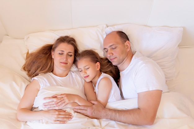 Familia feliz, mamá, papá, hija duermen en la cama en la habitación de