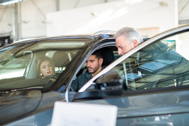 Familia Joven Feliz Hablando Con El Vendedor Y Eligiendo Su Nuevo Coche En Una Sala De 