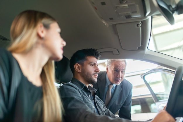 Familia Joven Feliz Hablando Con El Vendedor Y Eligiendo Su Nuevo Coche En Una Sala De 