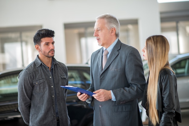 Familia Joven Hablando Con El Vendedor Y Eligiendo Su Auto Nuevo En Una Sala De Exposición 