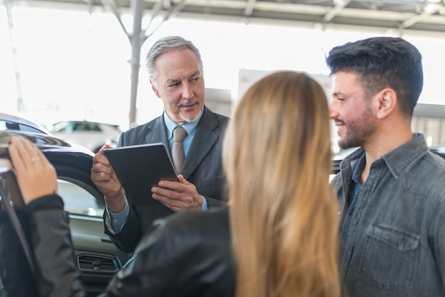 Familia Joven Hablando Con El Vendedor Y Eligiendo Su Nuevo Coche En Una Sala De Exposición 