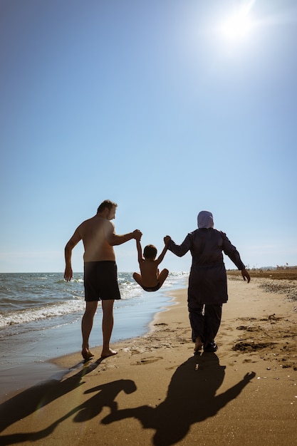 Familia musulmana papá y mamá con burkini en la playa caminando cerca