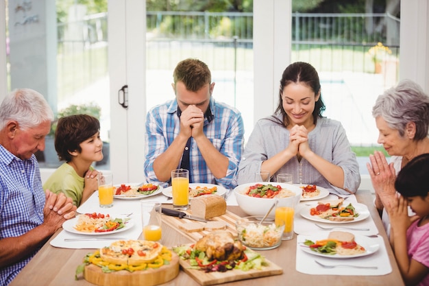 Familia sentada en la mesa del comedor y rezando juntos antes de comer |  Foto Premium