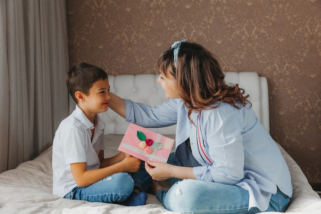 Feliz Día De La Madre Hijo Felicita A Mamá Y Le Da Una Postal Mamá Y Bebé Sonríen Y Se Abrazan 