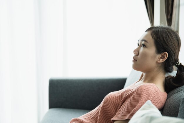 Feliz joven asiática relajándose en un sofá en la sala de estar mujer