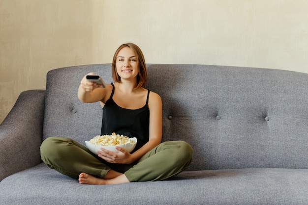 Feliz Linda Chica Sentada En El Sofá Gris Comiendo Palomitas De Maíz