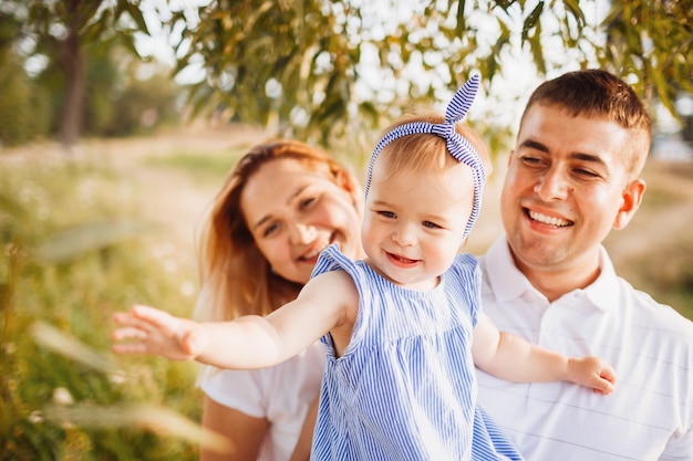 Feliz mamá y papá sostienen a pequeña hija en sus brazos de pie en los