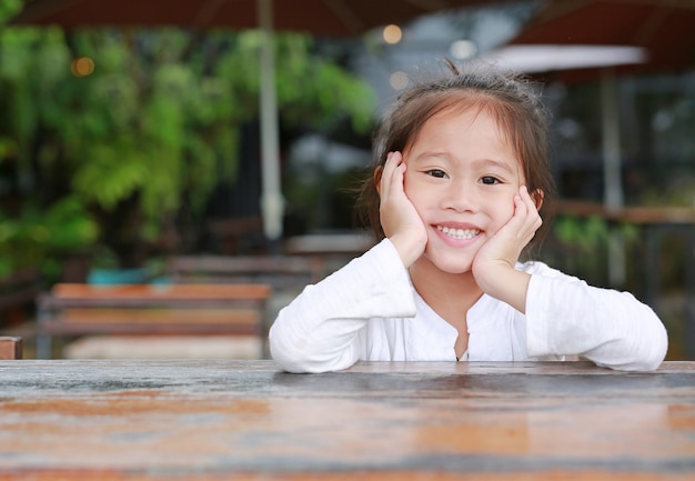 Foto Premium | Feliz niña asiática niño acostado en la mesa de madera con cámara