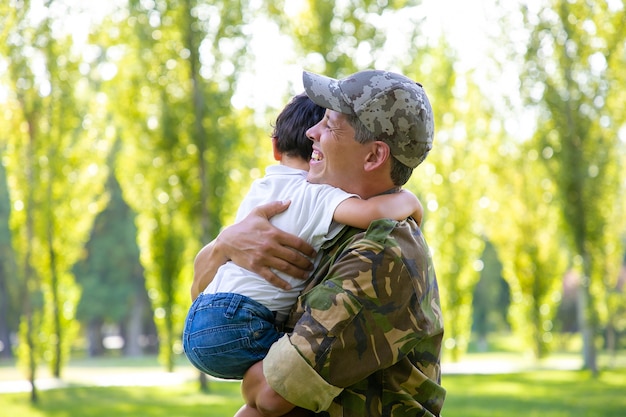 Feliz Papa Militar Reunido Con El Pequeno Hijo Despues Del Viaje Misionero Sosteniendo Al Nino En Brazos Y Sonriendo Reunion Familiar O Concepto De Regreso A Casa Foto Gratis