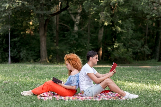 Feliz Pareja De Jóvenes Sentados Espalda Con Espalda En Una Manta De Picnic Foto Gratis 