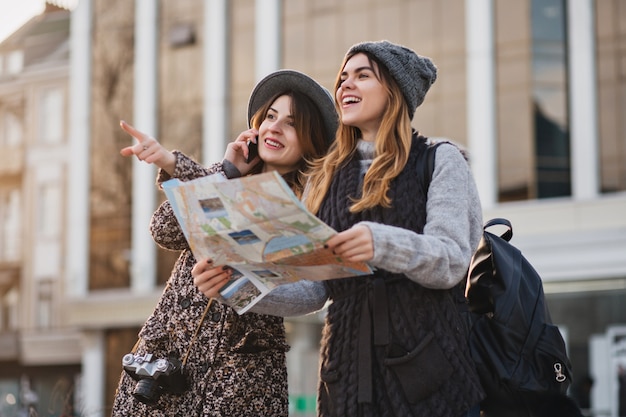 Feliz viaje juntos de dos mujeres de moda en el soleado centro de la ciudad. mujeres jóvenes alegres que expresan positividad, usando mapa, vacaciones con bolsas, emociones alegres, buen día. Foto gratis