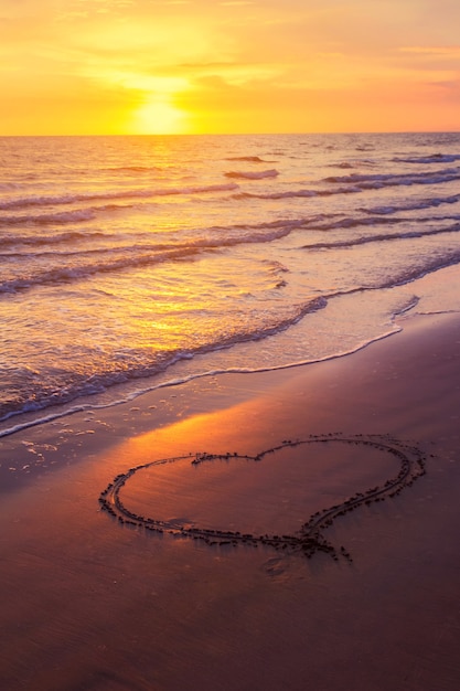 En forma de corazón dibujado en una playa de arena al atardecer Foto Premium