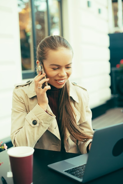 Foto De Una Mujer Joven Sentada En Un Café Hablando Con Su Teléfono Frente A Una Computadora Con 