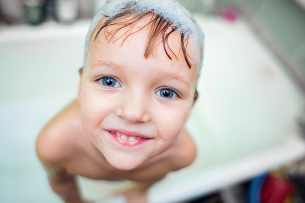 Gran retrato del niño bañándose en el baño con espuma en la cabeza