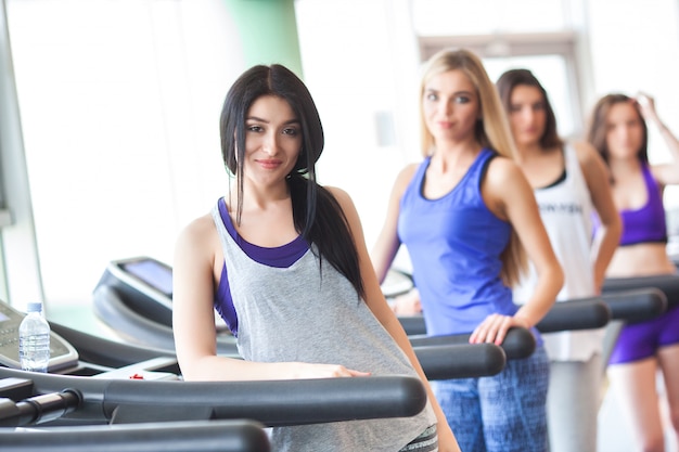 Un grupo de chicas guapas en buena forma corriendo en las cintas de correr. mujeres bonitas entrenando en el gimnasio. niña está sonriendo a la cámara Foto Premium