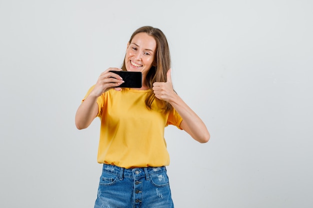 Hembra Joven Mostrando El Pulgar Hacia Arriba Mientras Toma Selfie En Camiseta Pantalones