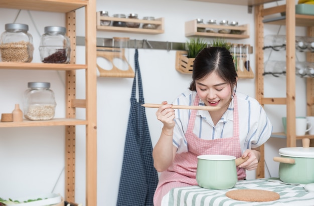 Hermosa joven asiática cocinando y probando comida de sopa en la cocina Foto Premium 
