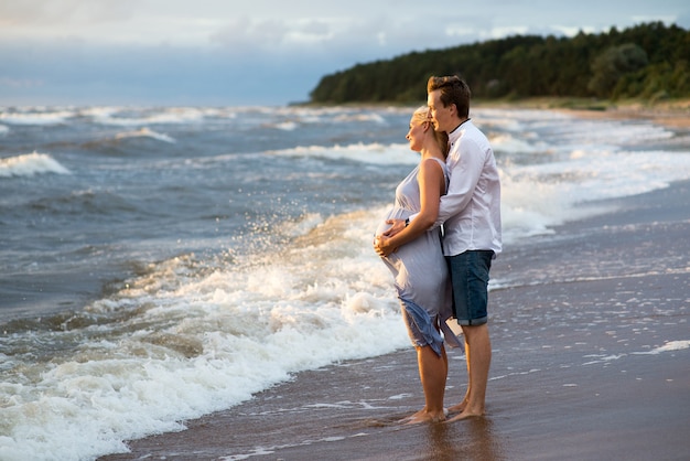 Una Hermosa Mujer Embarazada Con Su Esposo En La Playa Sonriendo Y Tocando Su Vientre Con Amor Y 1811