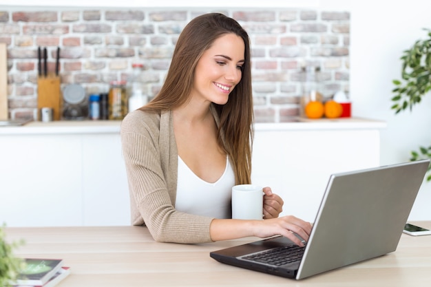 Hermosa mujer joven con su computadora portátil en la cocina ...