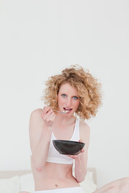 Hermosa Mujer Rubia Comiendo Un Plato De Cereales Mientras Está Sentado En Su Cama Foto Premium 