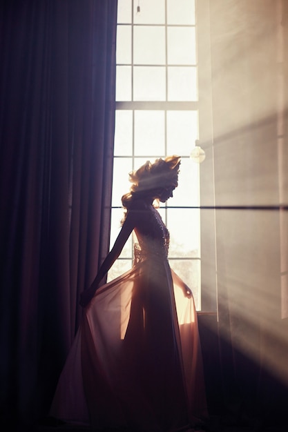 Hermosa mujer rubia de pie en la ventana de la luz del sol | Foto Premium