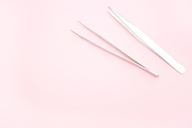 Herramientas para el procedimiento de extensión de pestañas. dos pinzas sobre fondo rosa. Foto Premium 