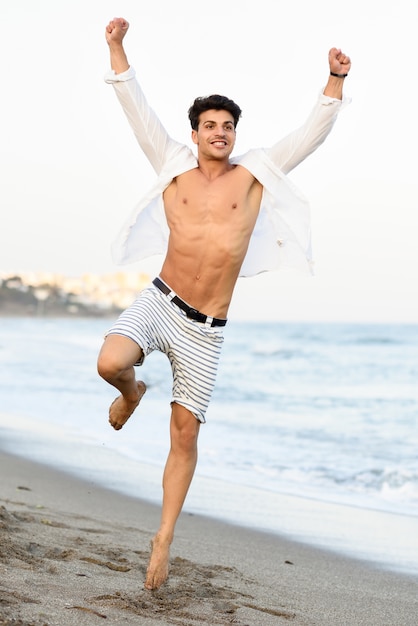 Hombre con la camisa abierta en la playa y una pierna levantada | Descargar Fotos gratis