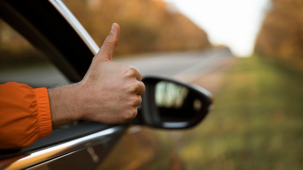 Hombre dando pulgares hacia arriba fuera de su coche durante un viaje